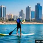Home 19 이스라엘에서의 해양 스포츠 - A serene scene of a young adult wearing a life jacket paddleboarding on calm Mediterranean waters ne...